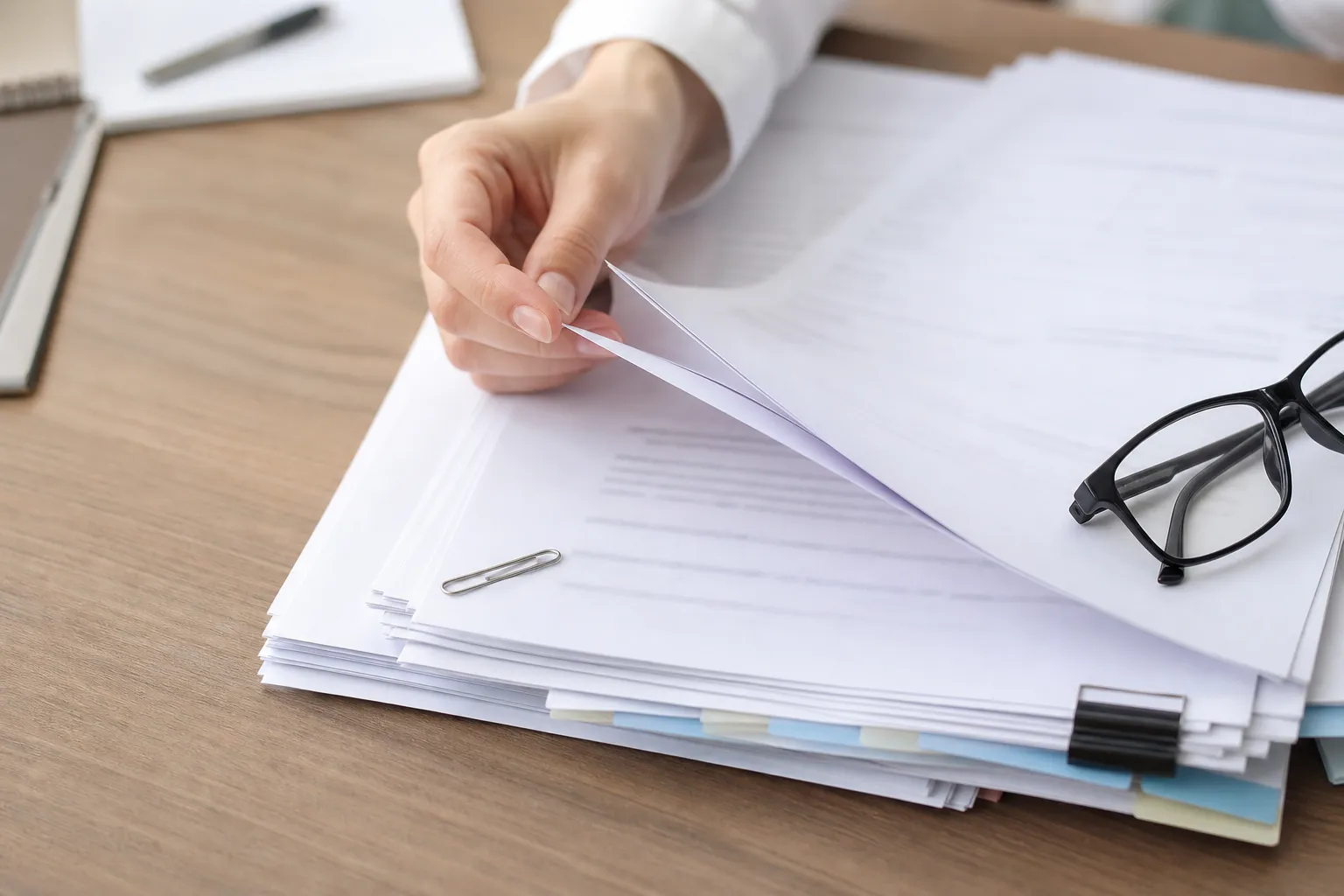 Documents administratifs empilés en éventail sur un bureau, trombone et lunettes posés dessus